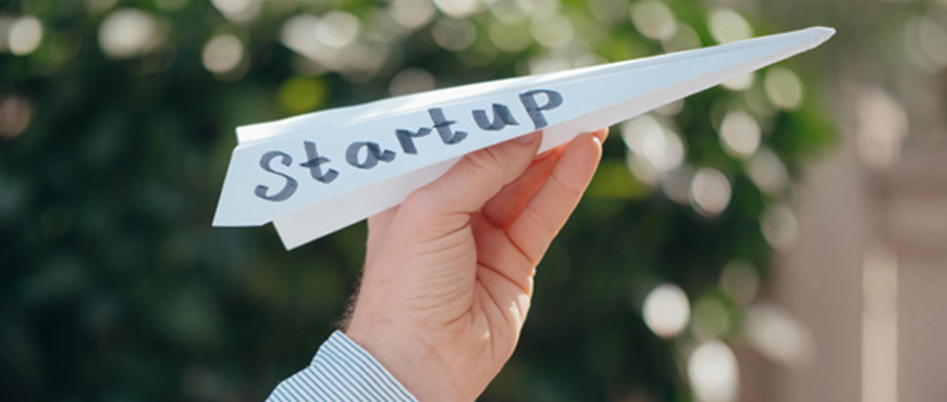 A hand holding a paper airplane that says "start up" on it.